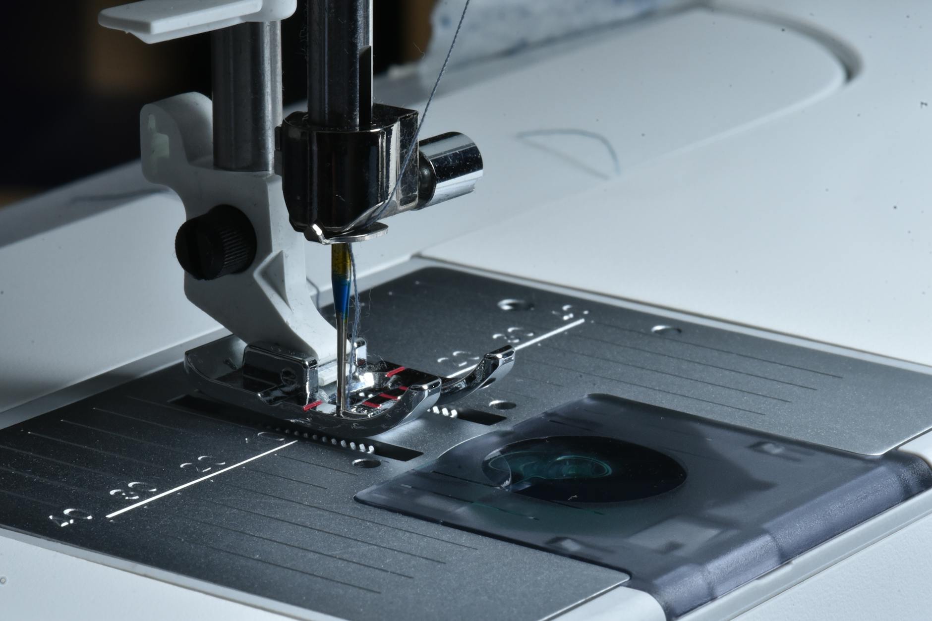 Prowadnik do szwów i taśma malarska: proste triki na równą linię Stopka i igła maszyny do szycia w zbliżeniu podczas szycia